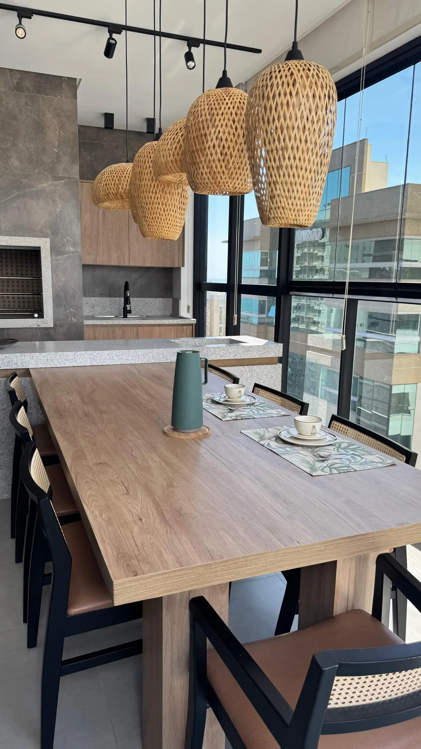 Mesa de madeira na sacada fechada com vidro, com pendentes de palha