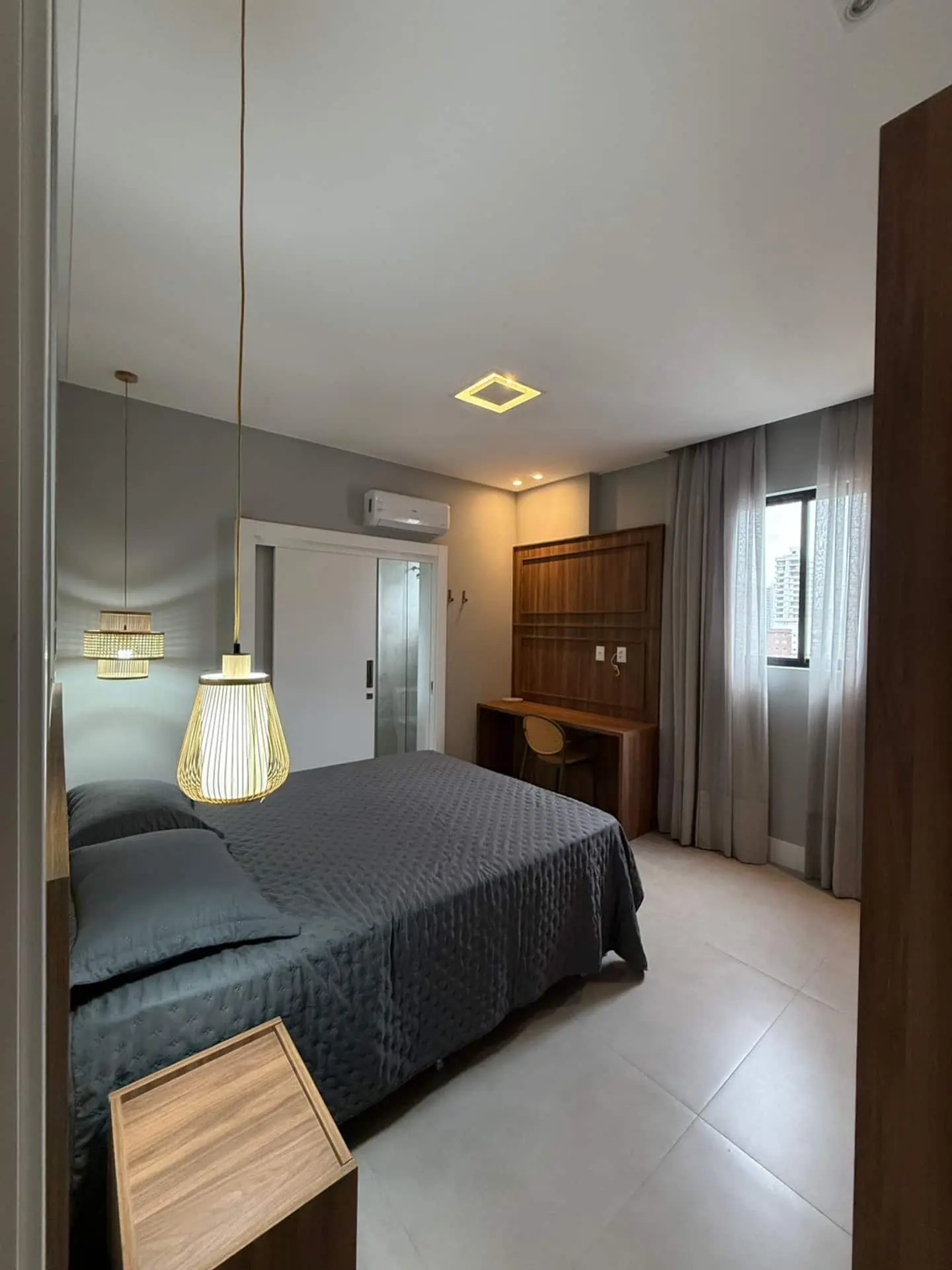 Suíte com roupa de cama escura, pendente de palha e mesa de trabalho