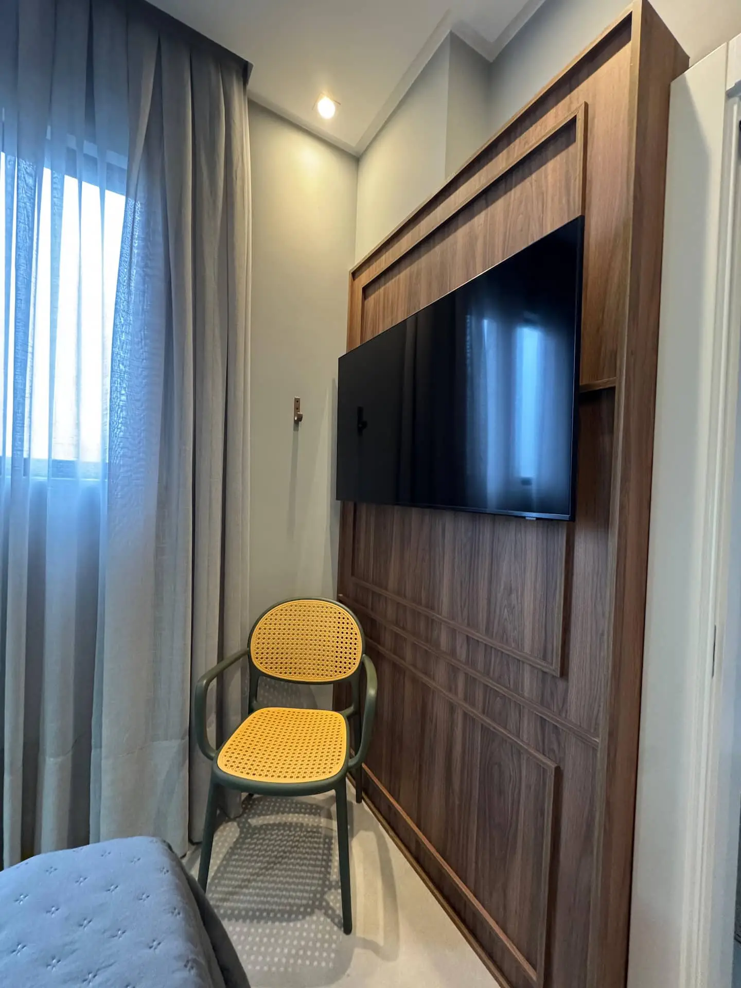 Painel de madeira com TV, cadeira amarela e cortina