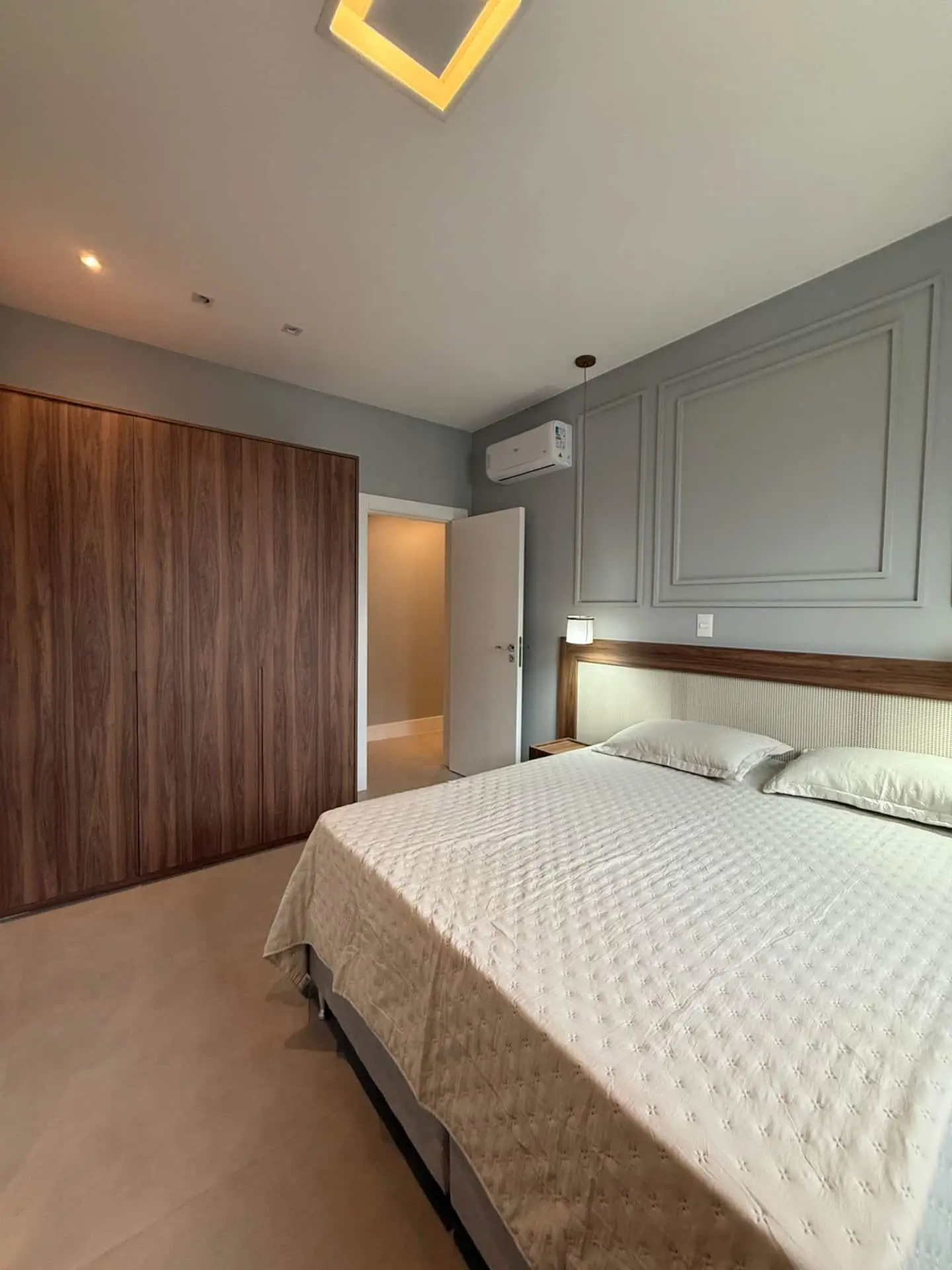 Suíte com armário de madeira e cama de colcha clara
