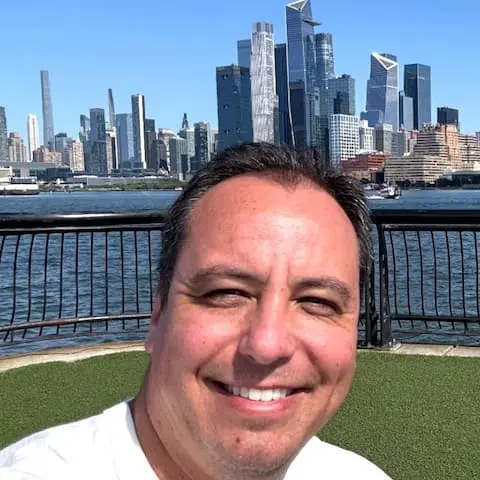 Fabriccio, anfitrião, sorrindo em frente à silhueta de uma cidade à beira da água
